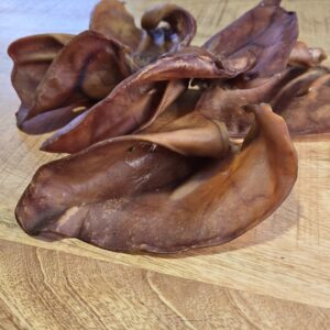 Oreille de porc naturelle posée sur une surface en bois, montrant sa texture et sa taille.