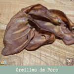 Oreille de porc naturelle posée sur une surface en bois, montrant sa texture et sa taille.