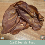 Oreille de porc naturelle posée sur une surface en bois, montrant sa texture et sa taille.