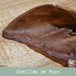 Oreille de porc naturelle posée sur une surface en bois, montrant sa texture et sa taille.